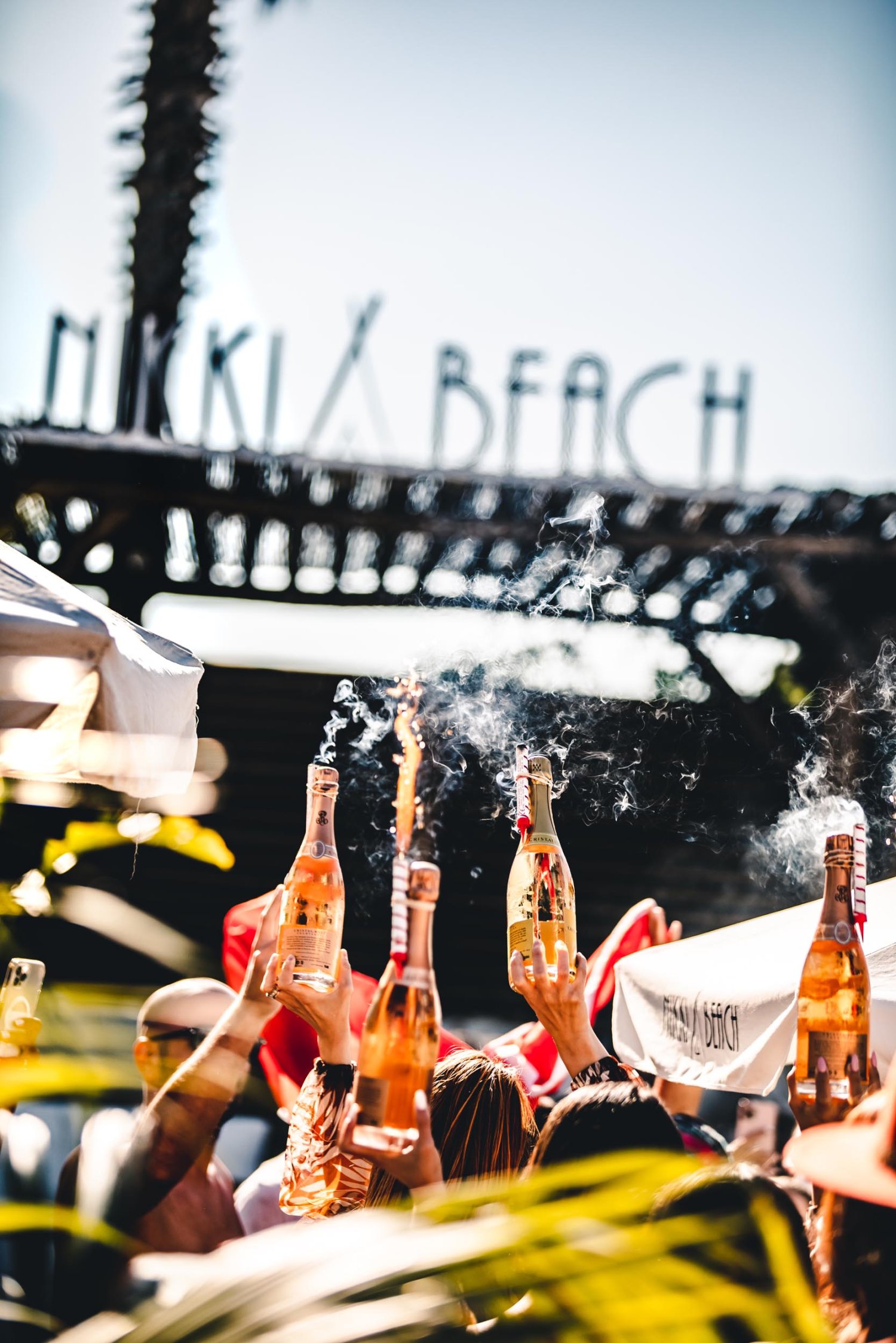 Nikki Beach party, a close up of guests holding bottles of wine in the air with sparklers attached