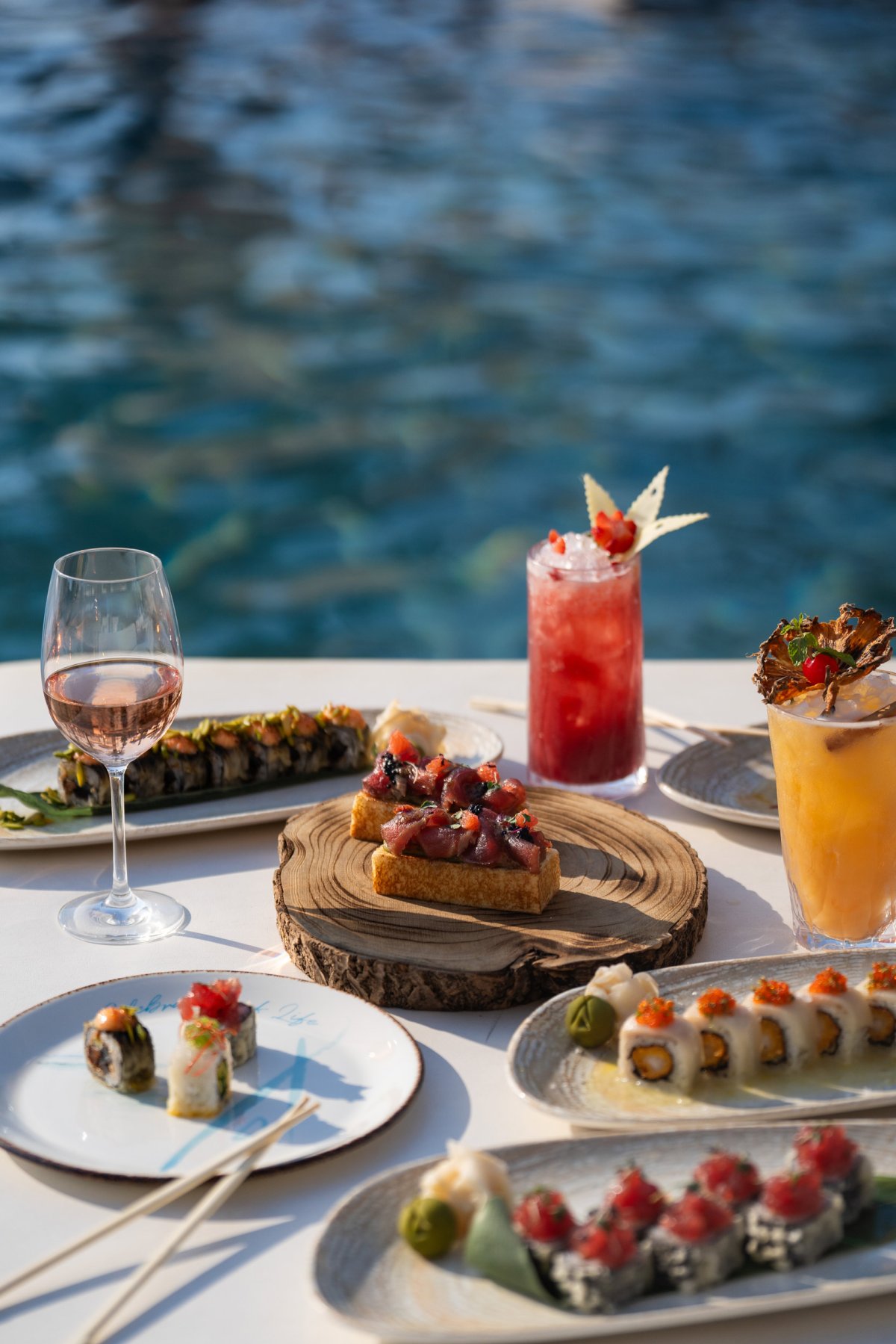 A table with cocktails and platters of sushi. The table is next to the pool