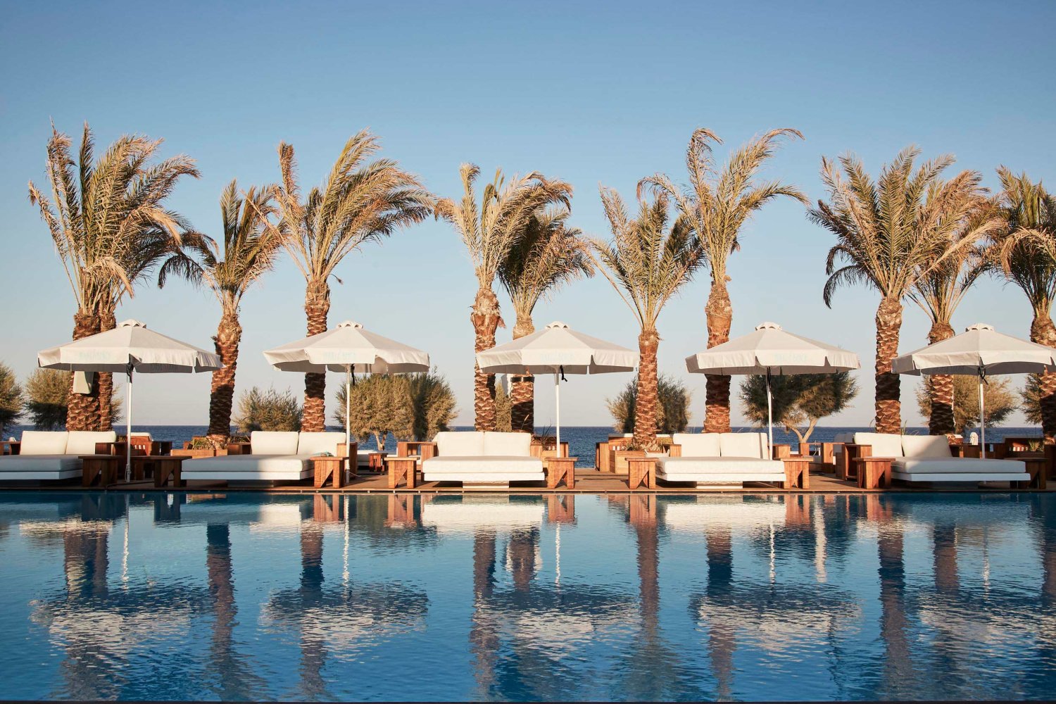 Image of Nikki Beach Santorini's pool with sofas and palm trees in the background