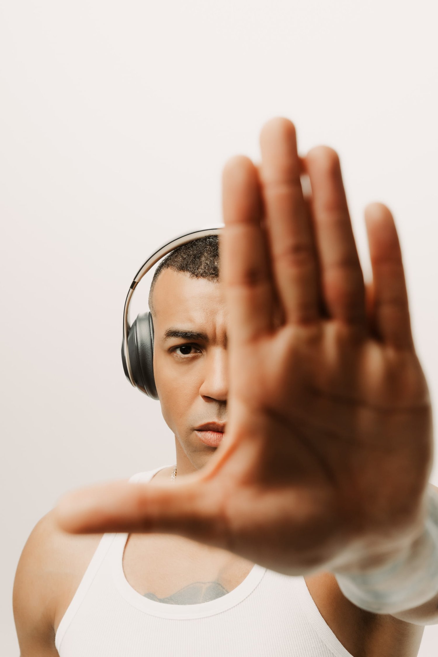 A striking studio portrait of special guest DJ Steve Provis wearing over-ear headphones and a white tank top. He looks intensely at the camera while holding his hand out toward the lens, partially obscuring his face. This bold image perfectly captures the dynamic energy he will bring to his set at the 