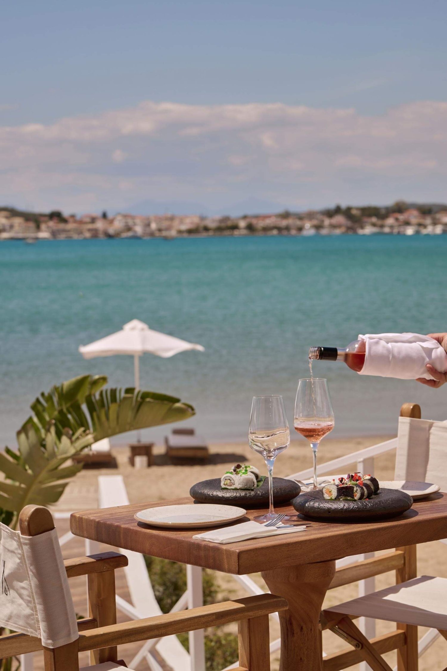 A waiter pouring a glasses of rosè at a table by the beach and sea