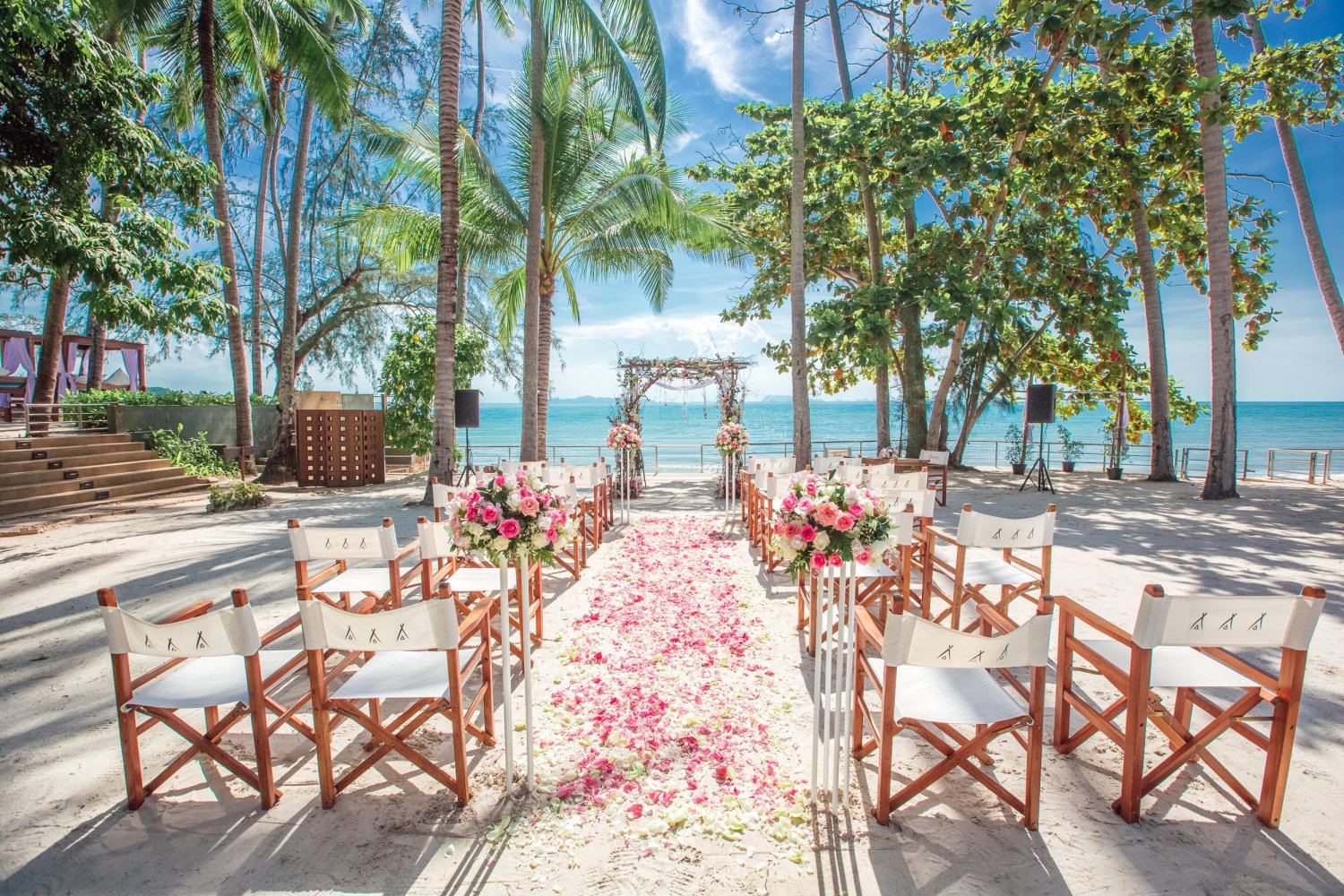 Shot of wedding isle along the beach with rose petals and chairs either side
